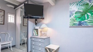 Habitació amb televisió, mirall, taula petita, banca i un mur amb una pintura de fulla tropical.