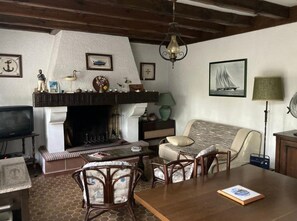A cozy living room with a fireplace, a sofa, a dining table, and various wall decorations. - Holiday Home 'Piraillan Foret' with Private Garden (Lège-Cap-Ferret)