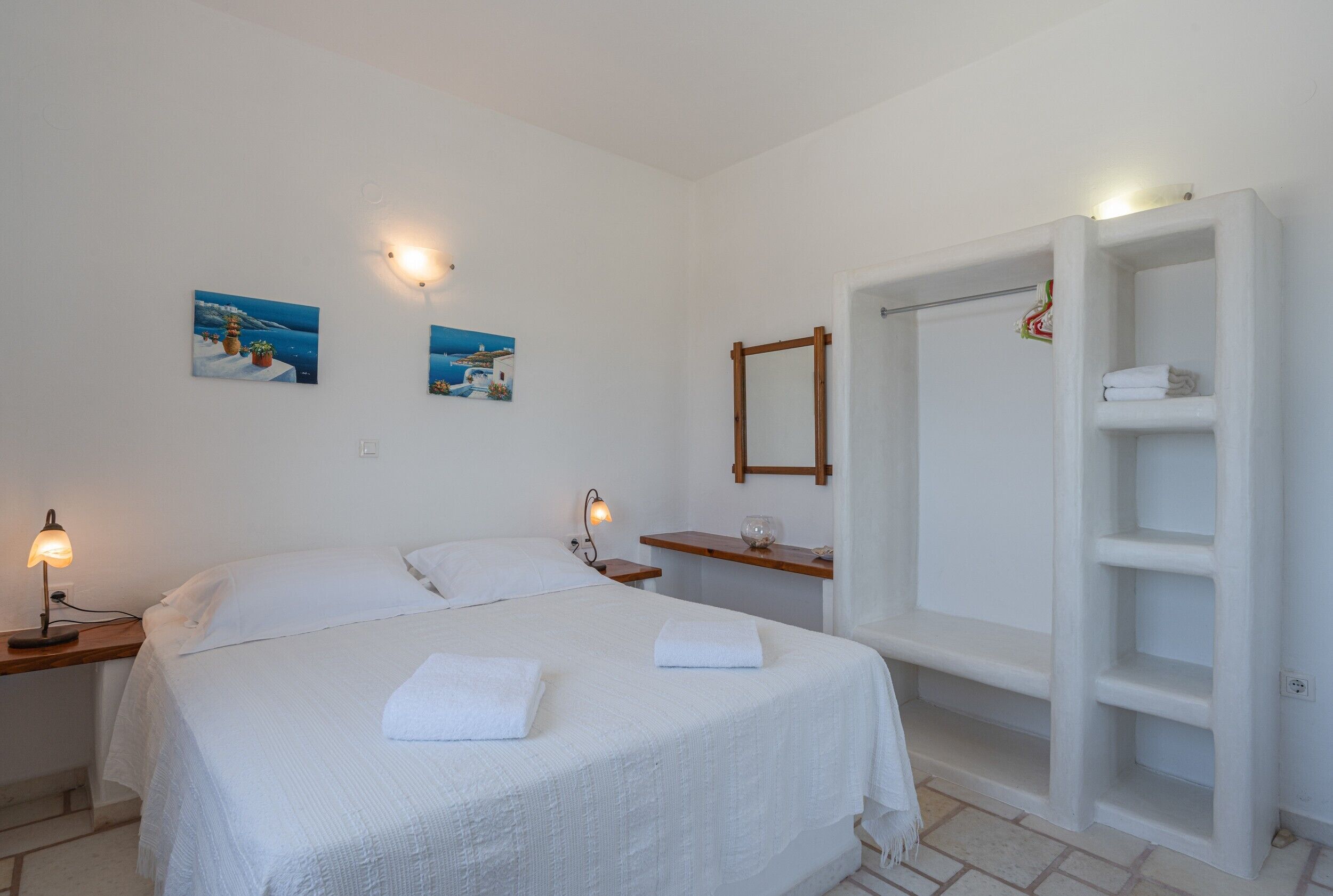 Een slaapkamer met een bed, bedlampjes, een nachtkastje, een houten plank, een spiegel en een inbouwkast.