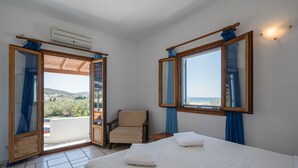 A bedroom with a bed, two towels, a chair, and a view through an open door. - Holiday Apartment "Maria's Village Suite" with Sea View, Private Terrace & Wi-Fi (Paros)