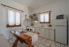 A compact kitchen with white cabinets, a wooden table, and a microwave.