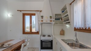 A compact kitchen with a stove, oven, sink, and a window with curtains. - Holiday Apartment "Maria's Village Suite" with Sea View, Private Terrace & Wi-Fi (Paros)