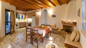 A dining area with a table set for four, wooden chairs, a sofa, and a fireplace with candles. - Vacation Home "Maria's Village Two Bedroom House 5" with Sea View, Terrace & Wi-Fi (Paros)