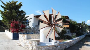 A windmill with a stone base, a white building with a stone facade, and a sign that reads 'Taverna Village.' - Vacation Home "Maria's Village Two Bedroom House 5" with Sea View, Terrace & Wi-Fi (Paros)