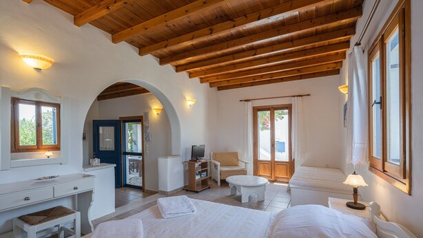 Une chambre avec un plafond en bois, un bureau, une chaise, une télévision et un lit.