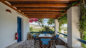 Une terrasse extérieure couverte, dotée d’un sol en pierre, d’une table avec des chaises, d’une porte bleue et d’un extincteur.