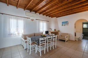 Um quarto acolhedor com teto de madeira, uma mesa de jantar com cadeiras, um sofá, uma televisão e uma máquina de lavar roupa.