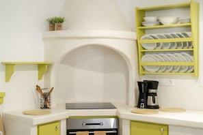 A kitchen with a built-in oven, a coffee maker, and a shelf with dishes.