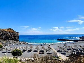 Una spiaggia con ombrelloni, una scogliera rocciosa e l'oceano.