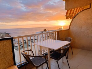 Ein Balkon mit Tisch und Stühlen, der Blick auf die Küste mit Gebäuden im Hintergrund freigibt.
