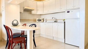 Una cocina moderna con armarios blancos, microondas integrado, estufa y refrigerador. Hay una mesa de comedor con sillas.