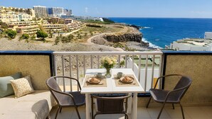 Un balcón con una mesa lista para dos personas, con vista al mar y edificios costeros.