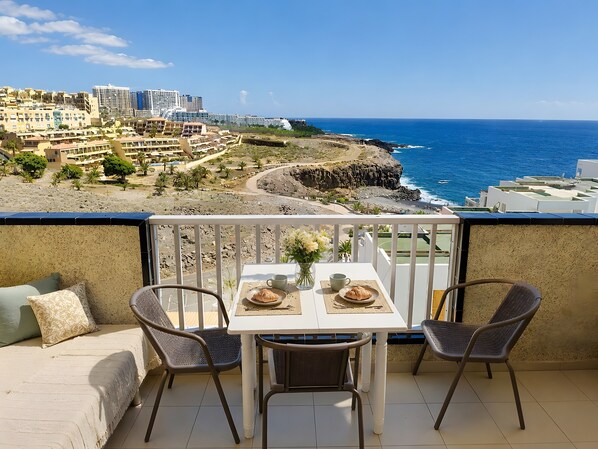 Ein Balkon mit Tisch für zwei Personen, mit Blick auf die Küste, Gebäude und das Meer.