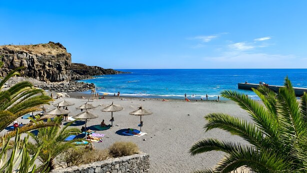 Una playa con un acantilado rocoso, sombrillas y gente tomando el sol.