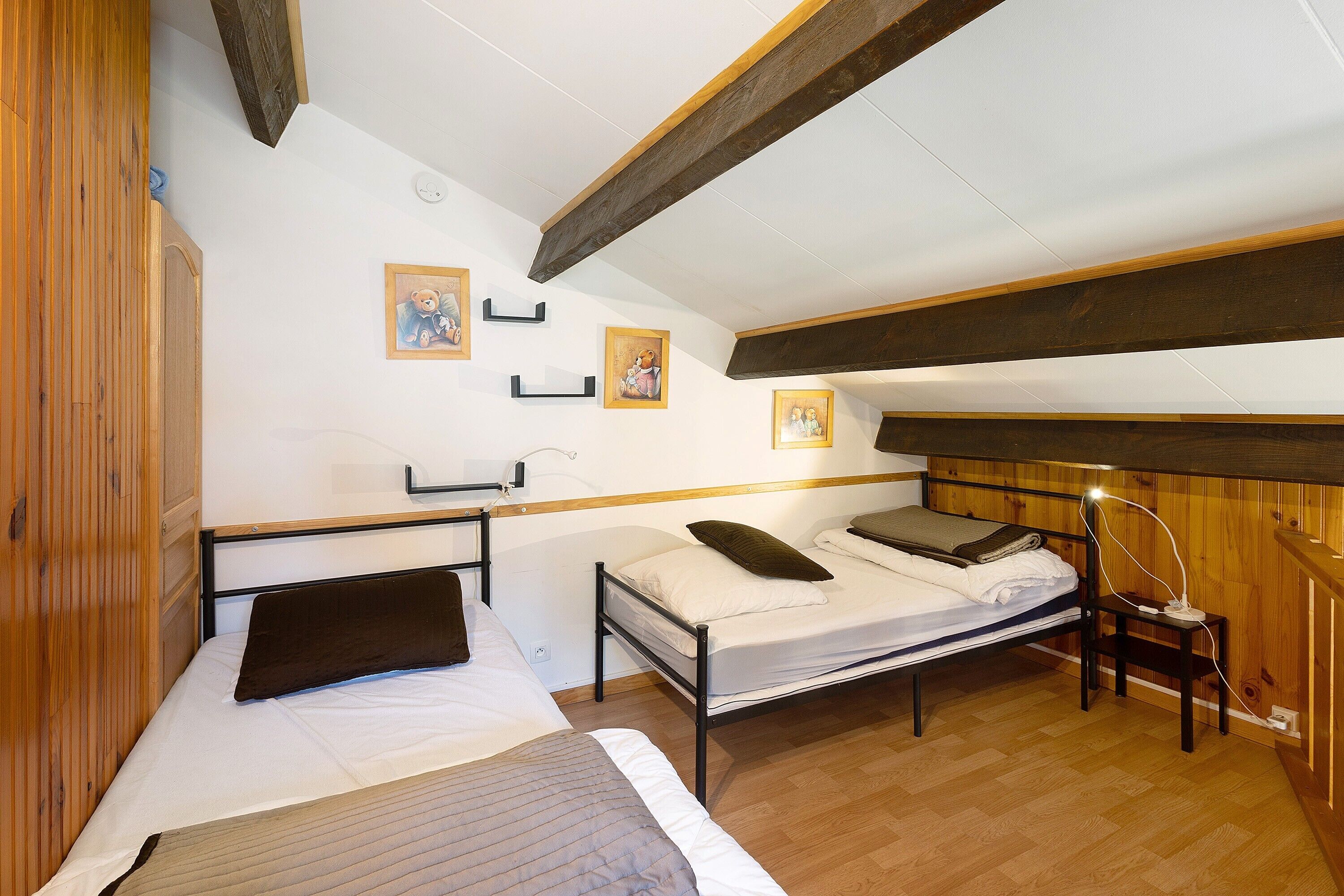 Una habitación con dos camas, vigas de madera, paredes blancas y cuadros enmarcados.