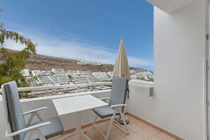 A balcony with a table and chairs, a view of a coastal town, and a mountain in the background.