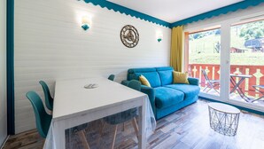 Une pièce avec une table blanche, des chaises turquoise, un canapé bleu, une horloge murale décorative et une vue sur une clôture rouge et de la verdure à l’extérieur.