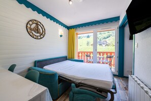 A bedroom with a bed, a table, chairs, a clock, and a view of the outdoors. - Apartment 'Appartement 4-6 Personnes' with Mountain View, Balcony and Wi-Fi (Saint-François-Longchamp)