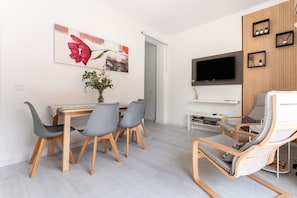 A modern living room with a dining table, chairs, a TV, and a sofa.