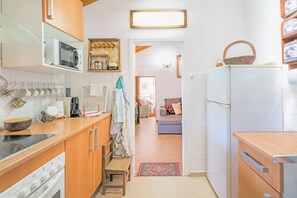 Cocina con microondas, estufa y armarios de madera. En el pasillo hay una silla y una alfombra.