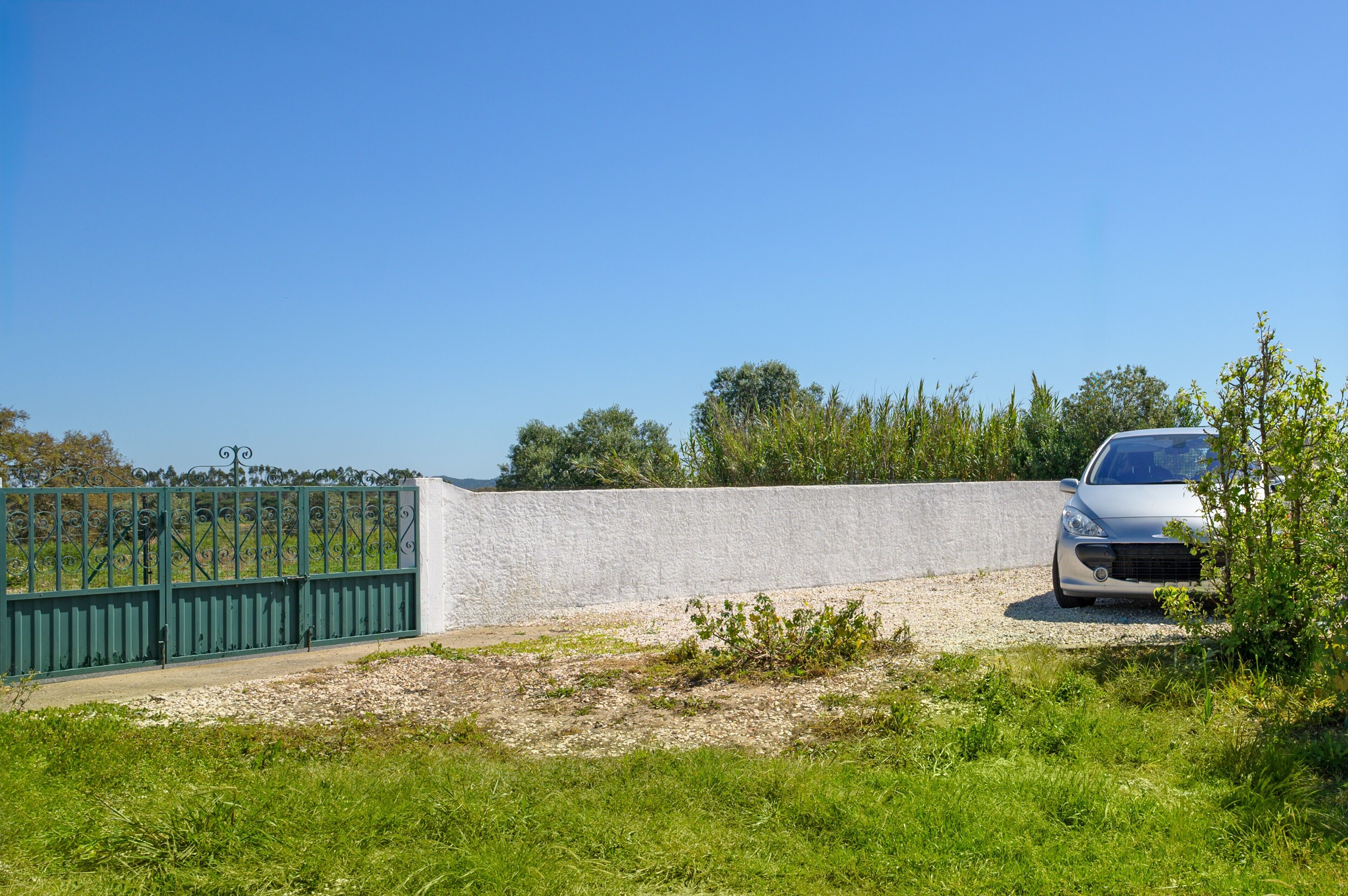 Een auto geparkeerd nabij een omheind gebied met een betonnen muur en begroeiing.