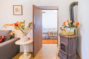 A room with a sofa, a small table with a vase of flowers, a wooden door, and a vintage stove. - Country House 'Monte Da Bárbara' with Private Terrace, Garden and Wi-Fi (Algoceira)