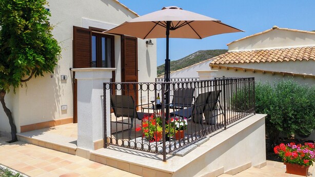 A patio with a table, chairs, and an umbrella. There are potted plants and a railing around the patio. - Appartamento Alba - Le 3 Rose Apartments (Sicilia)