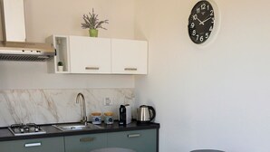 A compact kitchen with a gas stove, sink, and modern appliances. There is a dining table with chairs and a clock on the wall. - Appartamento Alba - Le 3 Rose Apartments (Sicilia)