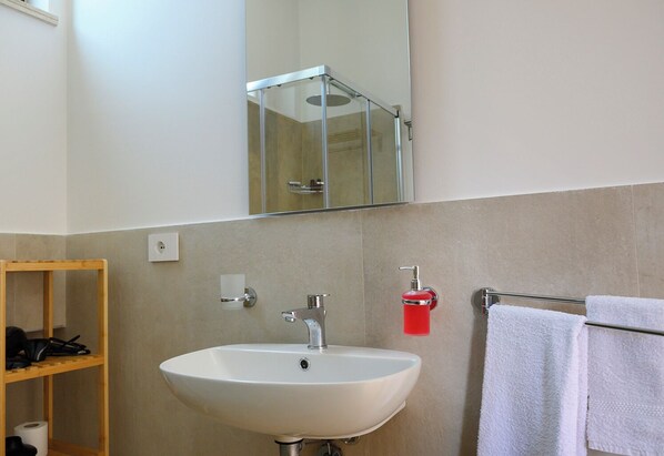A bathroom with a white sink, a mirror, a towel rack, and a wooden shelf. - Appartamento Alba - Le 3 Rose Apartments (Sicilia)