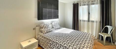 A bedroom with a bed, a nightstand, a chair, and a window with curtains.