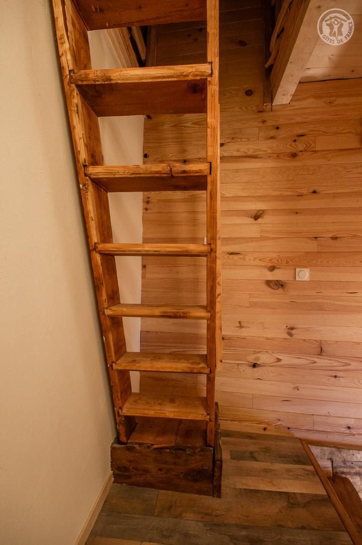 Une étagère en forme d’échelle en bois, adossée à un mur en bois, avec un escalier en arrière-plan.
