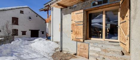 A building with a wooden balcony and a large glass door, surrounded by snow.