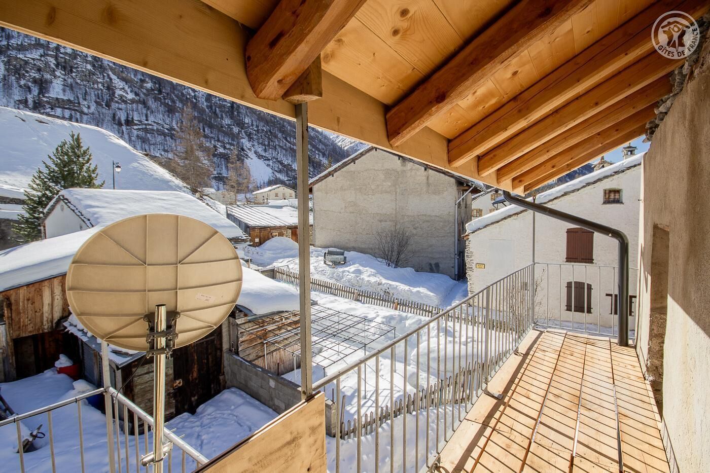 A wooden balcony with a view of snow-covered houses and mountains.
