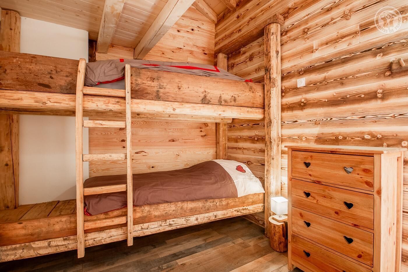A wooden cabin room with a bunk bed, a dresser, and a small bedside table.