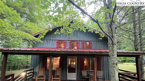 A rustic cabin with a porch, wooden chairs, and a red roof.