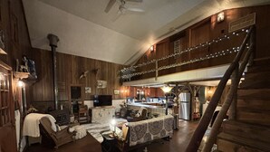A spacious loft-style living area with a high ceiling, wooden walls, and a mezzanine.