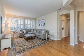 A spacious living room with a grey sofa, a patterned rug, and a painting on the wall.