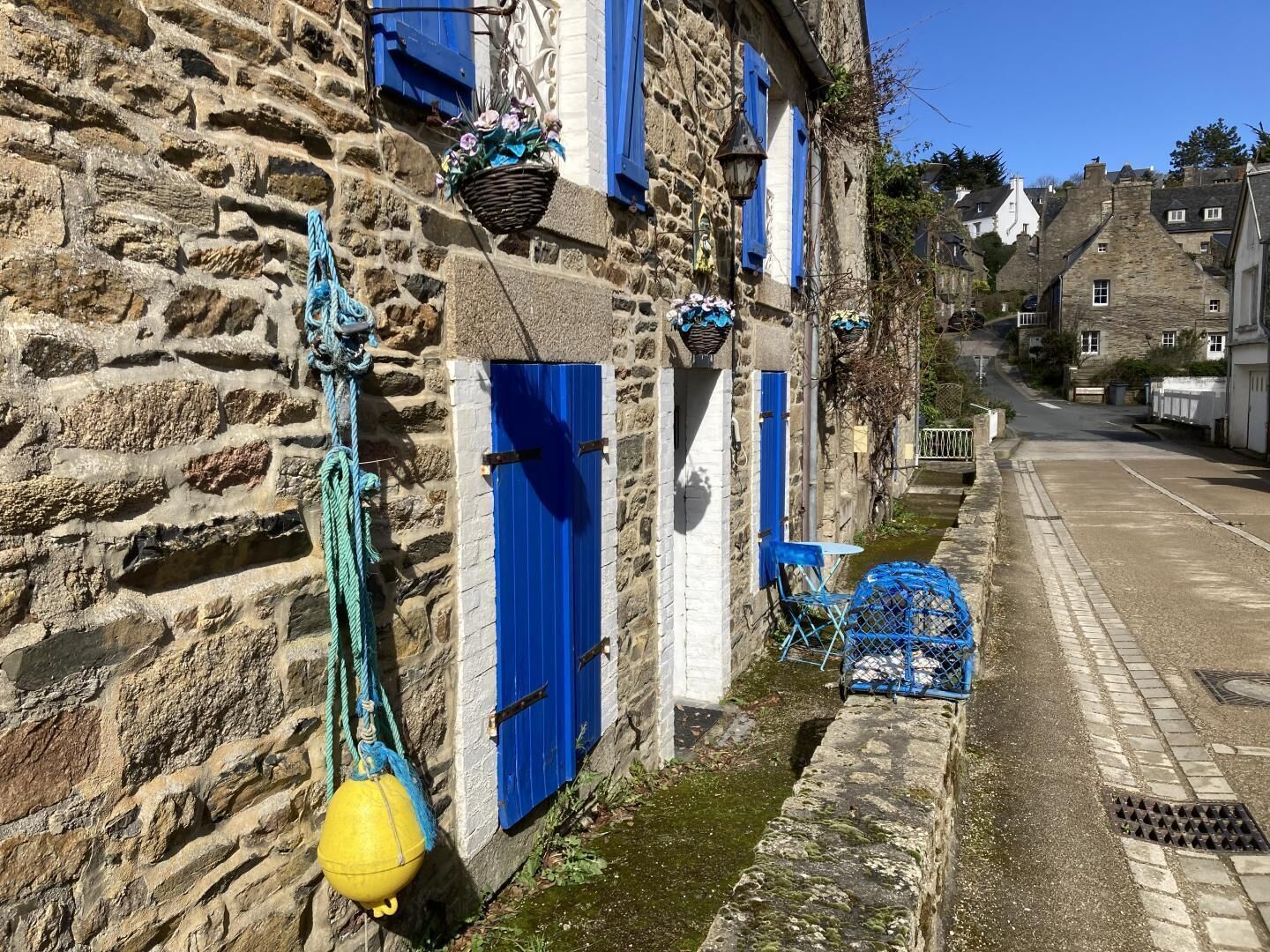 A stone building with blue shutters, a yellow buoy, and a narrow street.