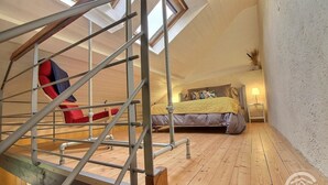 A bedroom with a wooden floor, a bed with a yellow blanket, a red chair, and a skylight.