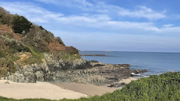 A coastal landscape with rocky cliffs, a sandy beach, and the ocean.
