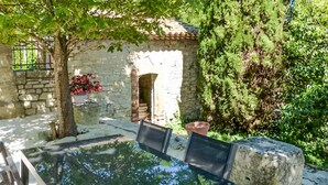 An outdoor patio with a glass table and chairs, a stone wall, and a small archway.