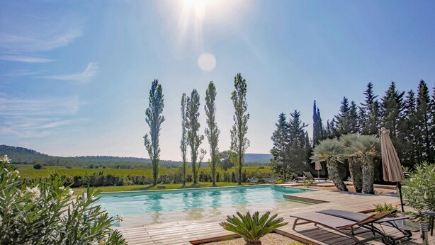 A pool area with a wooden deck, lounge chairs, and a view of a green landscape with trees and hills in the background.