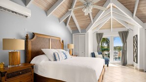Ein Schlafzimmer mit einem hölzernen Bett, zwei Nachttischlampen, einem Deckenventilator und Blick ins Freie durch eine Glastür.