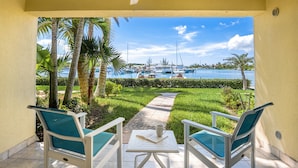 Eine Terrasse mit zwei Stühlen und einem Tisch, mit Blick auf eine Marina mit Booten und Palmen.