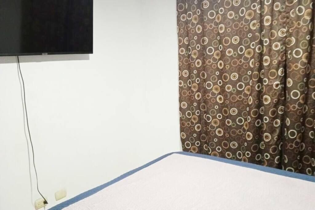 Une chambre avec un lit, un téléviseur fixé au mur et un rideau à motifs.