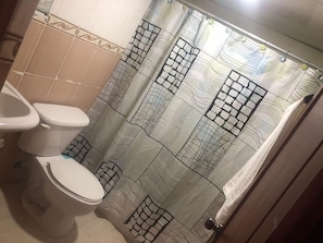 A bathroom with a toilet, a shower curtain with a geometric pattern, and tiled walls.