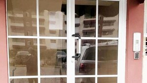 En glasdør med håndtag og et tastatur, samt et spejlbillede af en bygning og en parkeret bil.