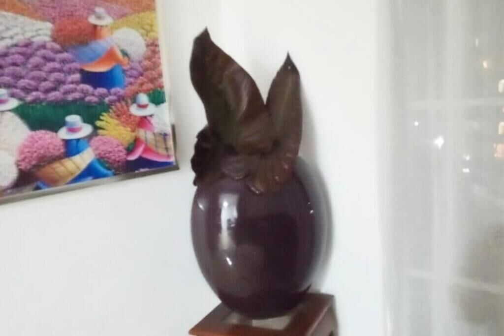 A dark-colored vase with a leaf design on a wooden stand.