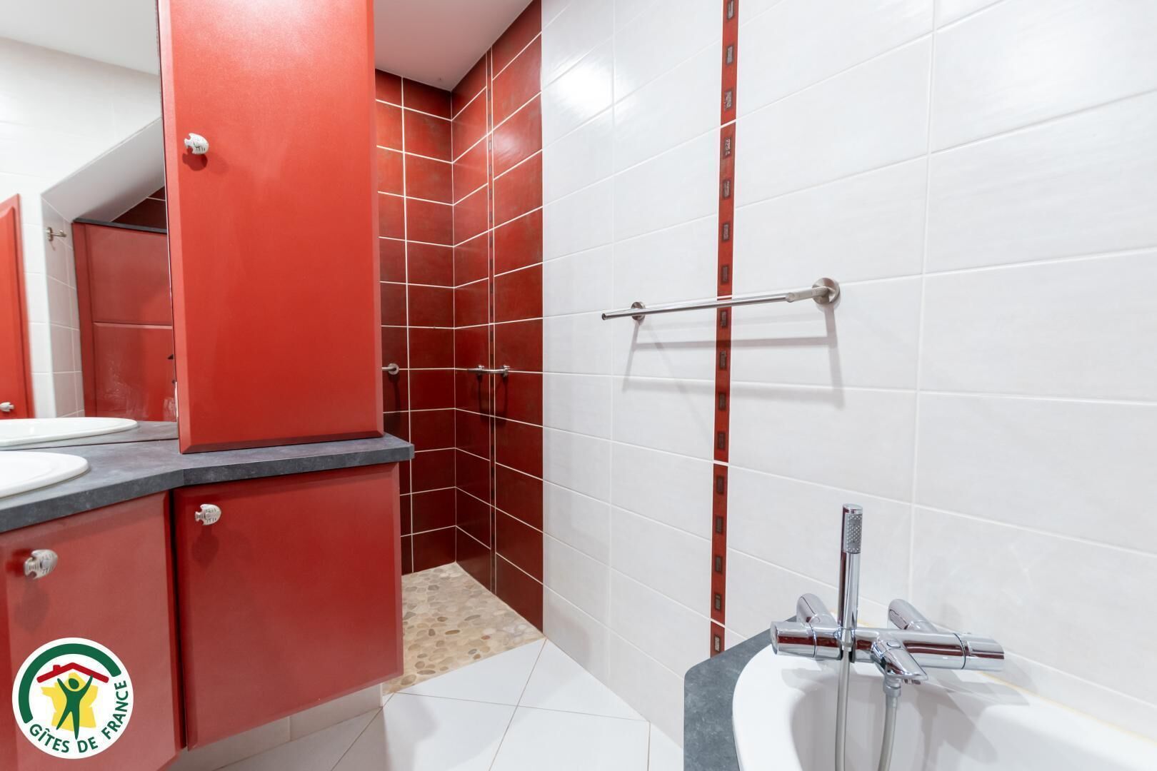 A bathroom with a red and white tiled shower area, a white sink, and a bathtub with a chrome faucet.