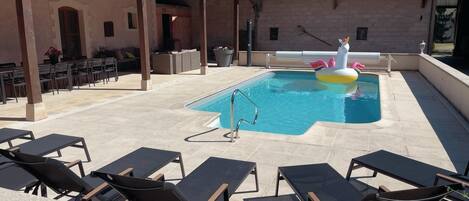A pool area with lounge chairs, a pool, and a building with a tiled roof.